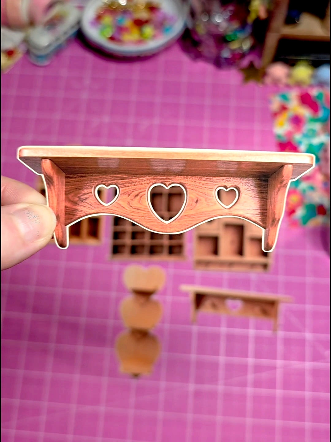 Small wooden shelf with heart cutouts held by a hand on a pink checkered background