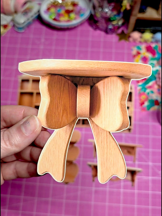 Wooden stool with a small round platform held by a hand on a pink grid background.
