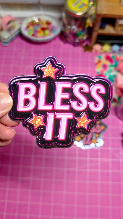 Pink 'BLESS IT' patch held in front of a pink background with toys.