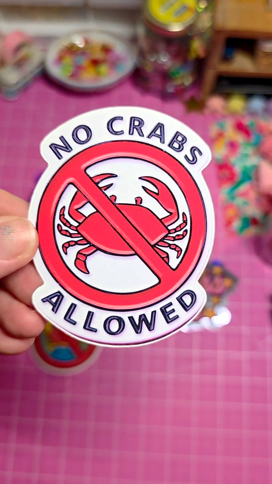 Sticker with 'No Crabs Allowed' design held over a colorful background