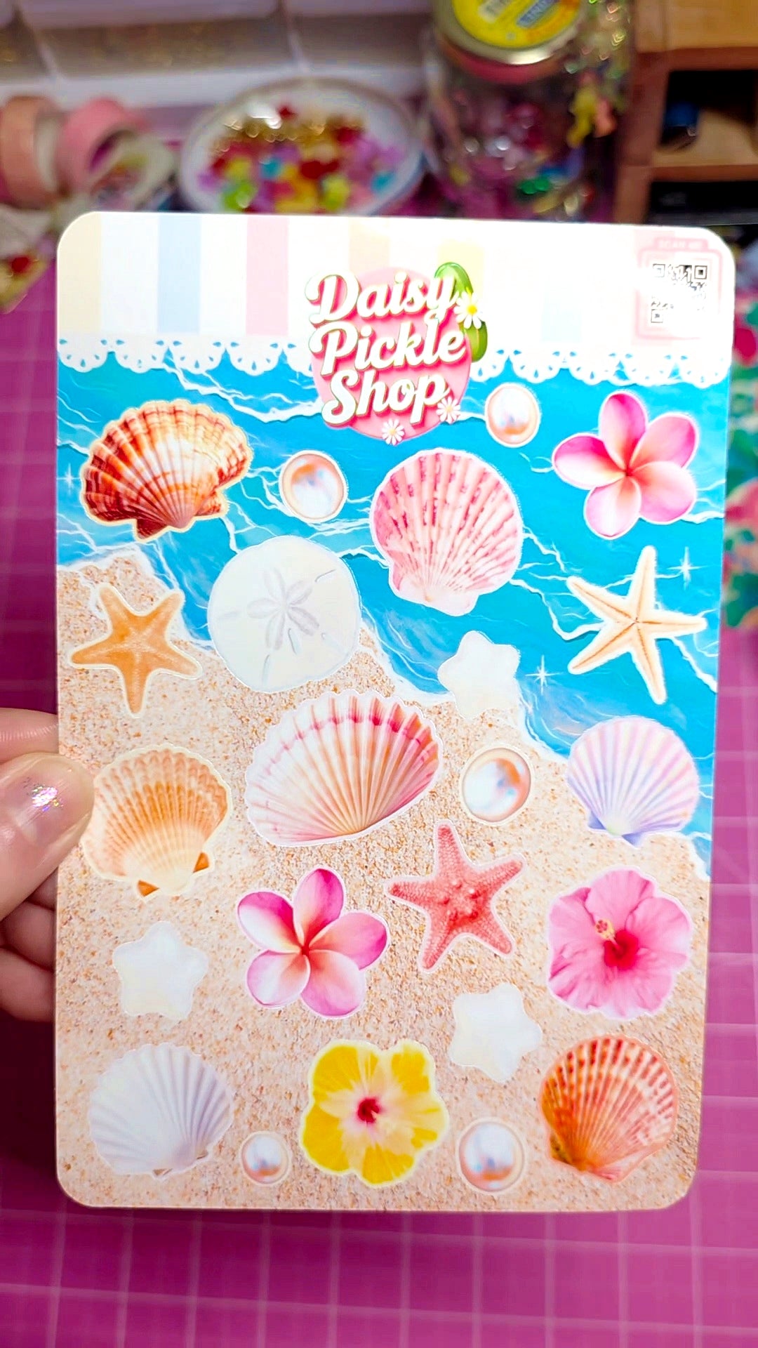 Sticker sheet with sea-themed designs held by a hand on a pink surface.